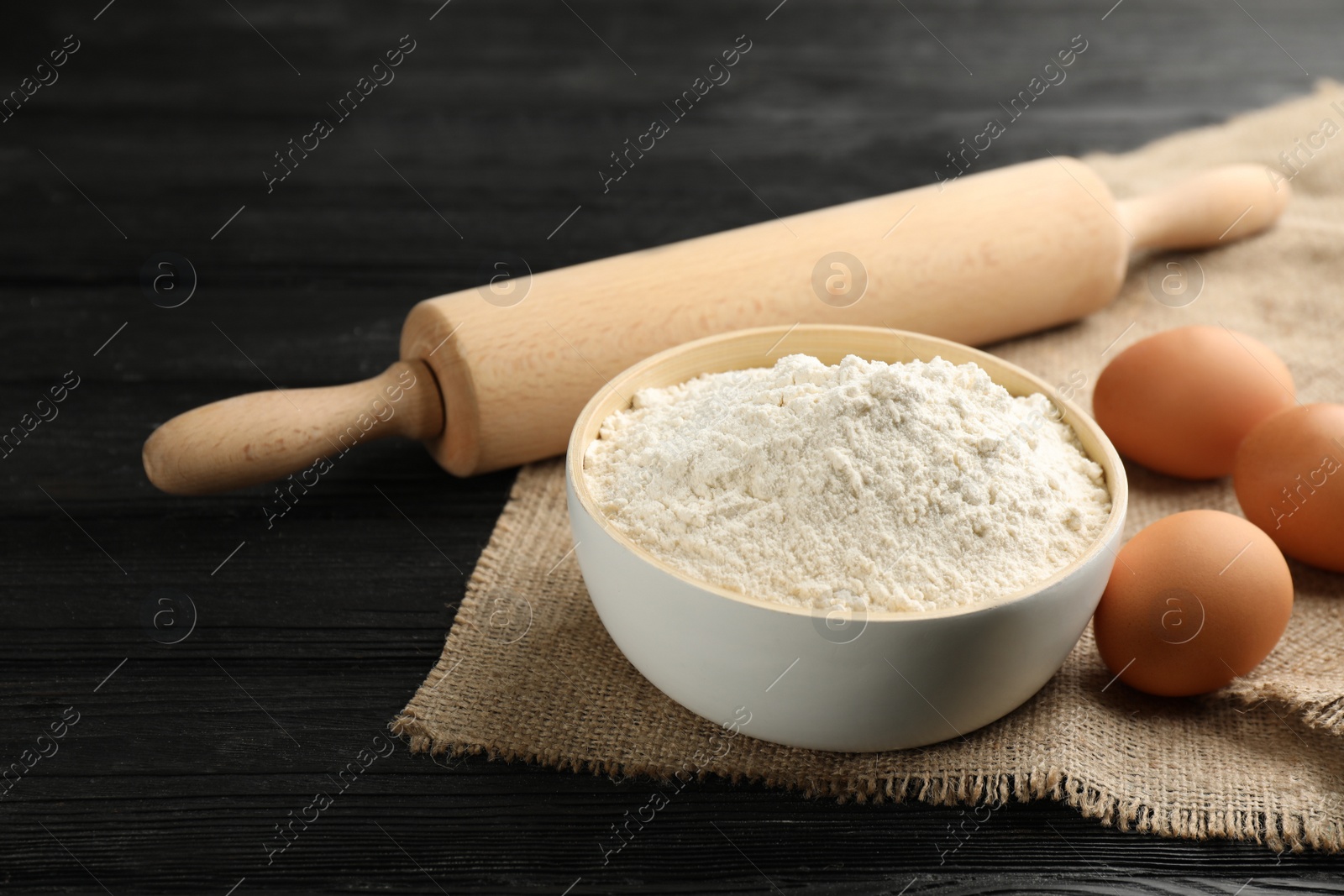 Photo of Bowl of flour, eggs and rolling pin on black wooden table