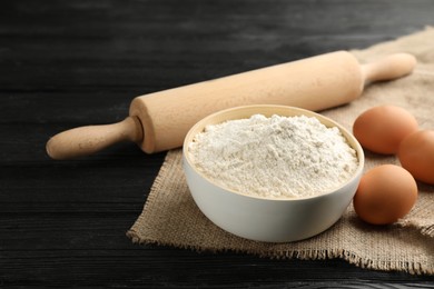 Photo of Bowl of flour, eggs and rolling pin on black wooden table