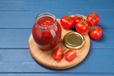 Photo of Organic ketchup in jar and fresh tomatoes on blue wooden table. Tomato sauce
