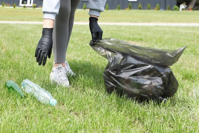 Photo of Woman with trash bag picking up glass and plastic bottles outdoors, closeup. Recycling concept