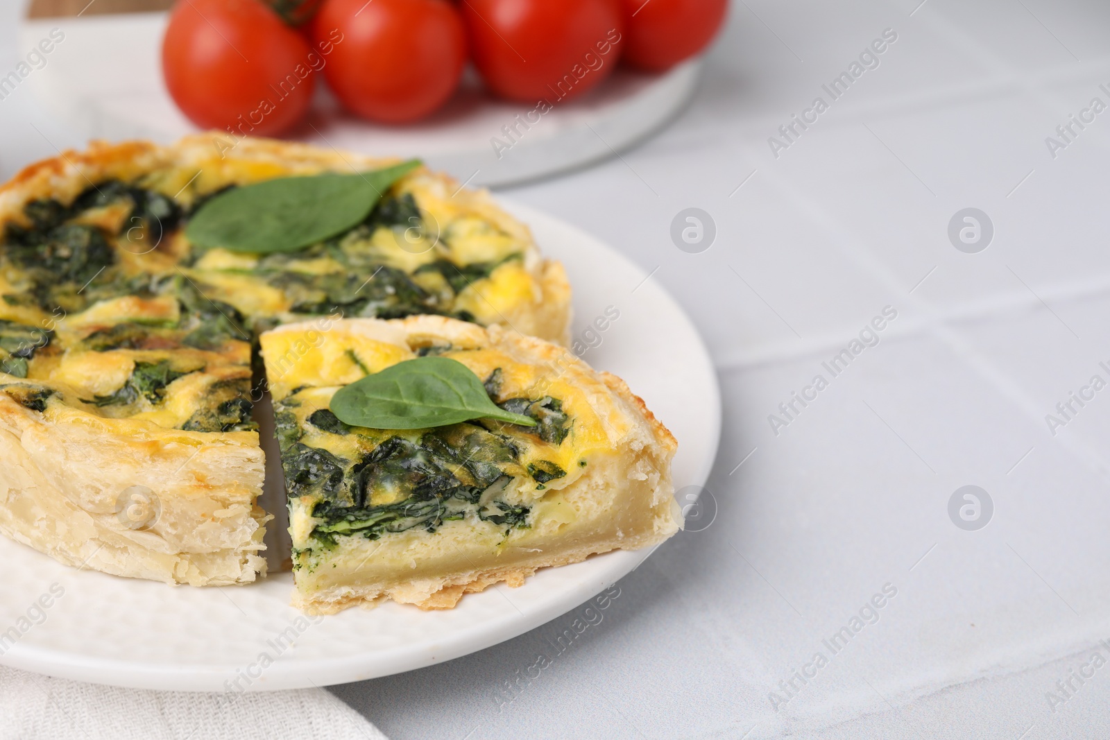 Photo of Delicious pie with spinach on white tiled table, closeup. Space for text