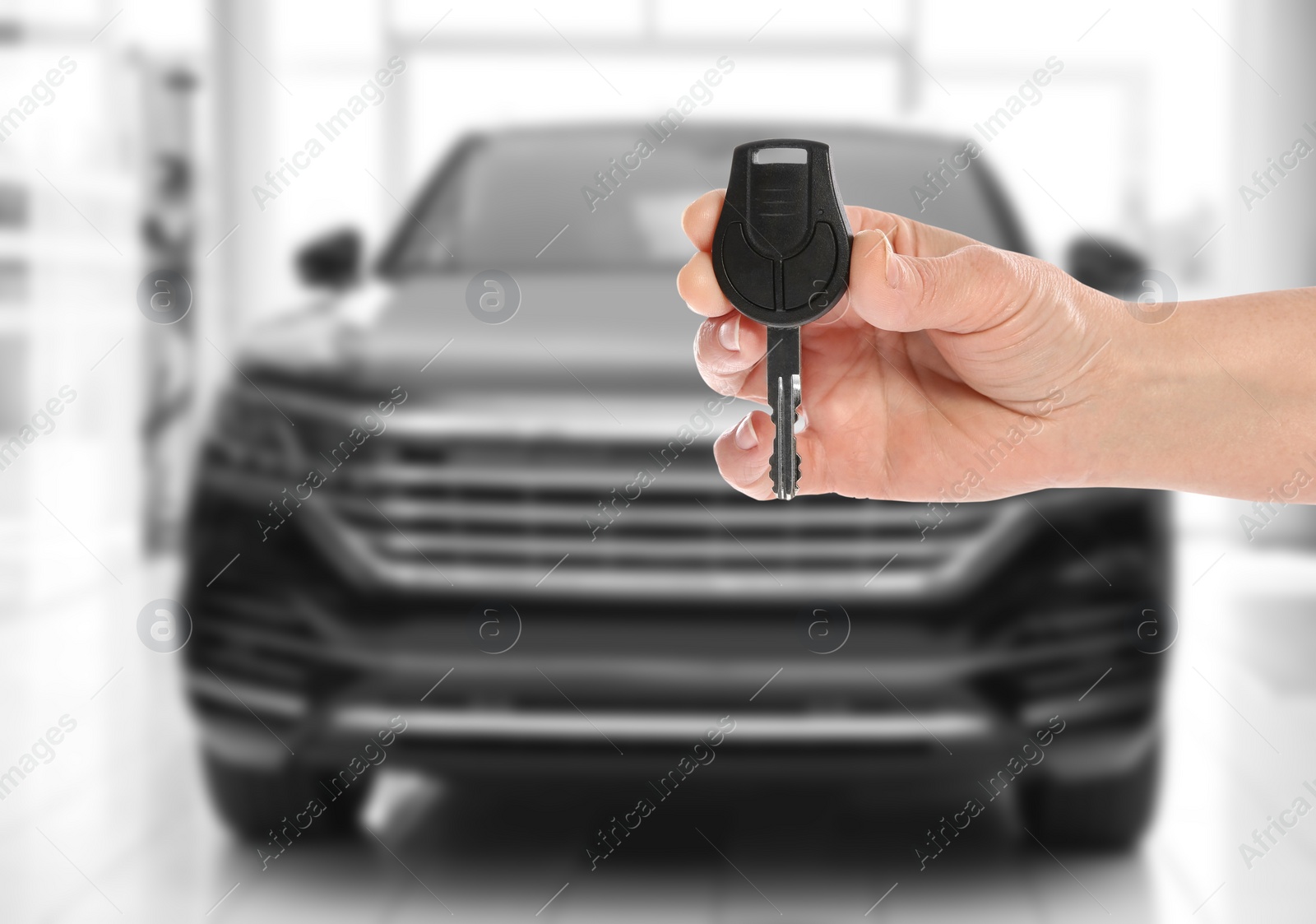 Image of Car buying. Woman holding key against blurred automobile, closeup