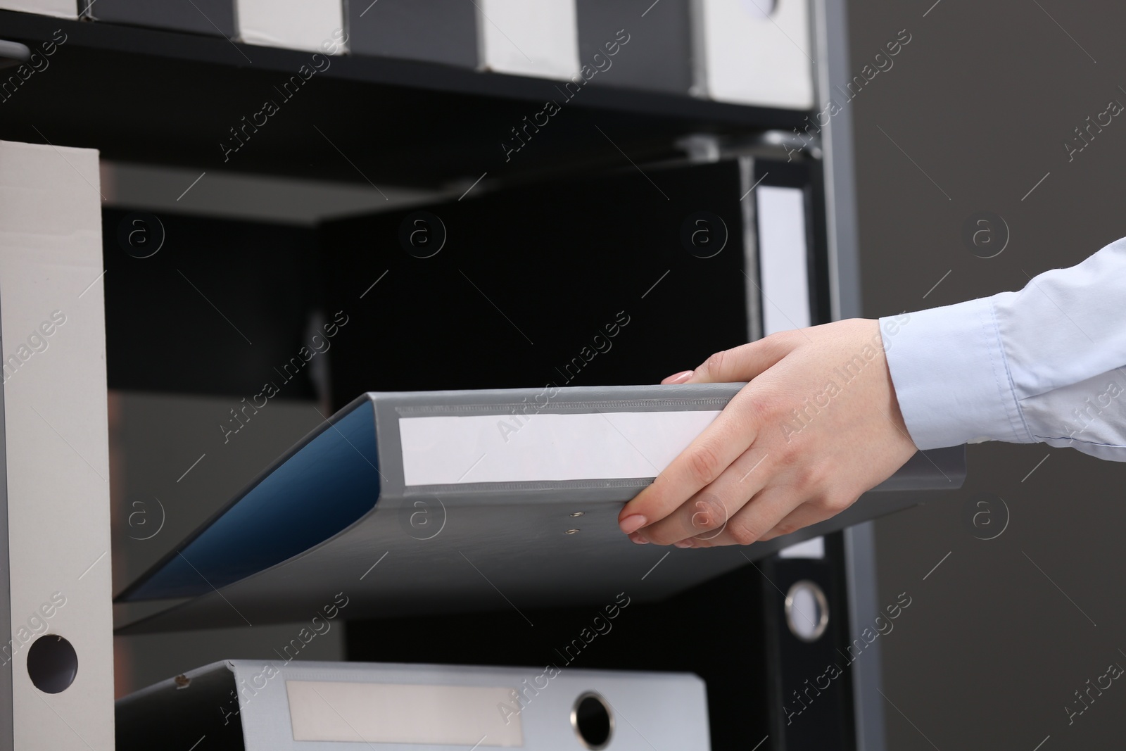 Photo of Woman taking folder with documents from shelf in office, closeup