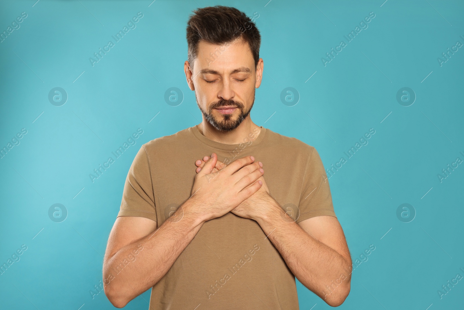 Photo of Man with clasped hands praying on turquoise background