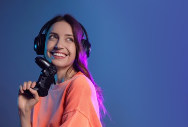 Photo of Happy woman in headphones with game controller on dark blue background