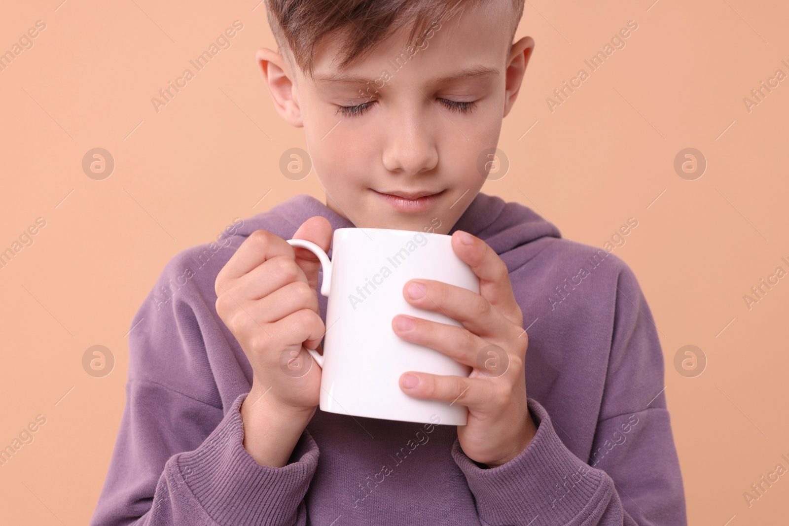 Photo of Cute boy with white ceramic mug on beige background