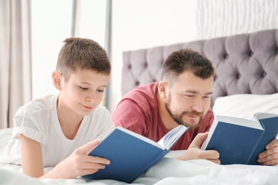 Photo of Little boy and his dad reading books in bedroom