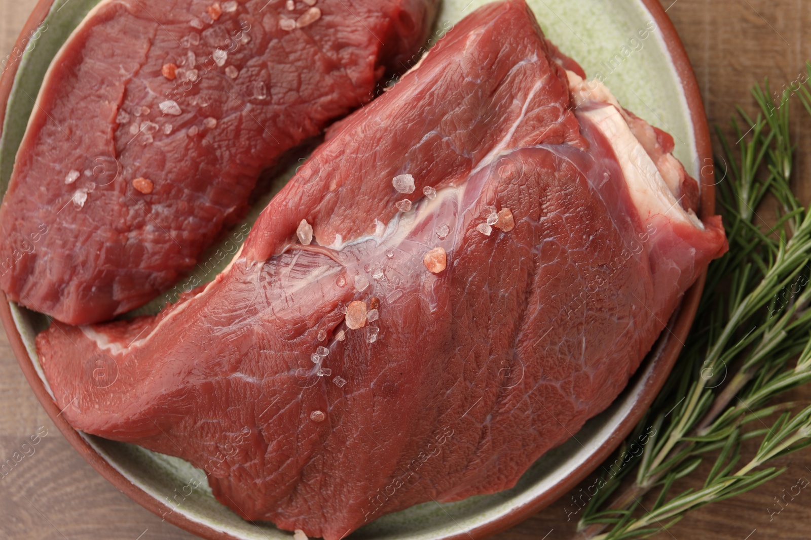 Photo of Pieces of raw beef meat with spices and rosemary on table, flat lay