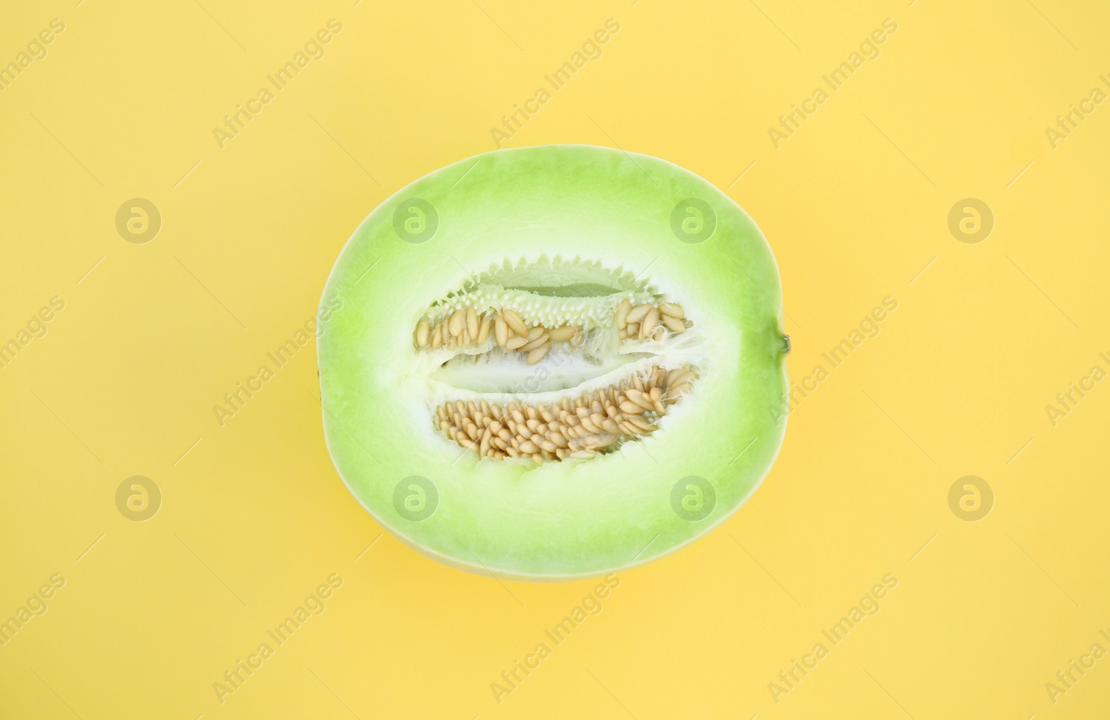 Photo of Half of fresh ripe honeydew melon on yellow background, top view