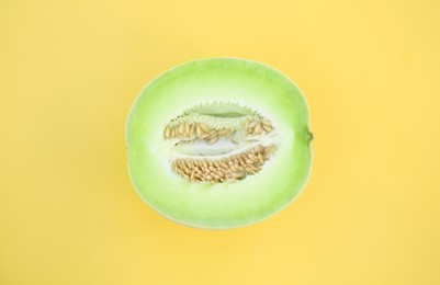 Photo of Half of fresh ripe honeydew melon on yellow background, top view