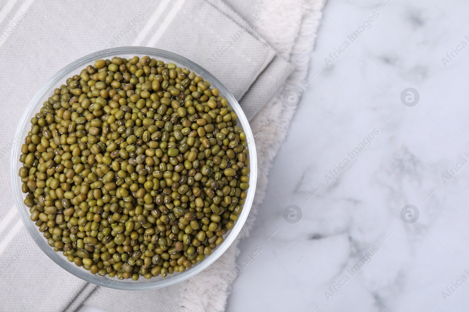 Photo of Glass bowl with green mung beans on white marble table, top view. Space for text