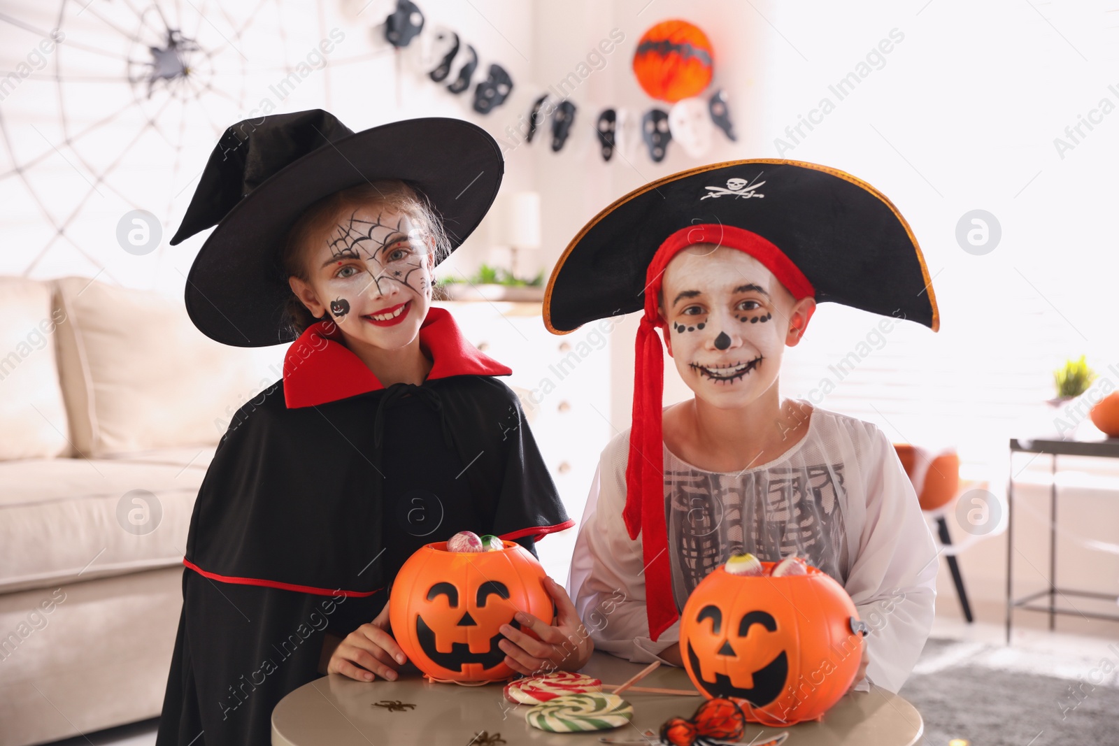 Photo of Cute little kids with pumpkin candy buckets wearing Halloween costumes at home