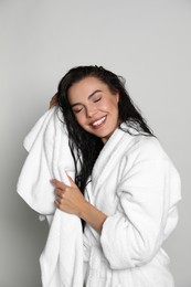Photo of Beautiful young woman in bathrobe drying hair with towel on light background