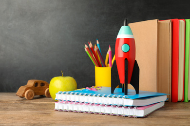 Photo of Bright toy rocket and school supplies on wooden desk. Space for text