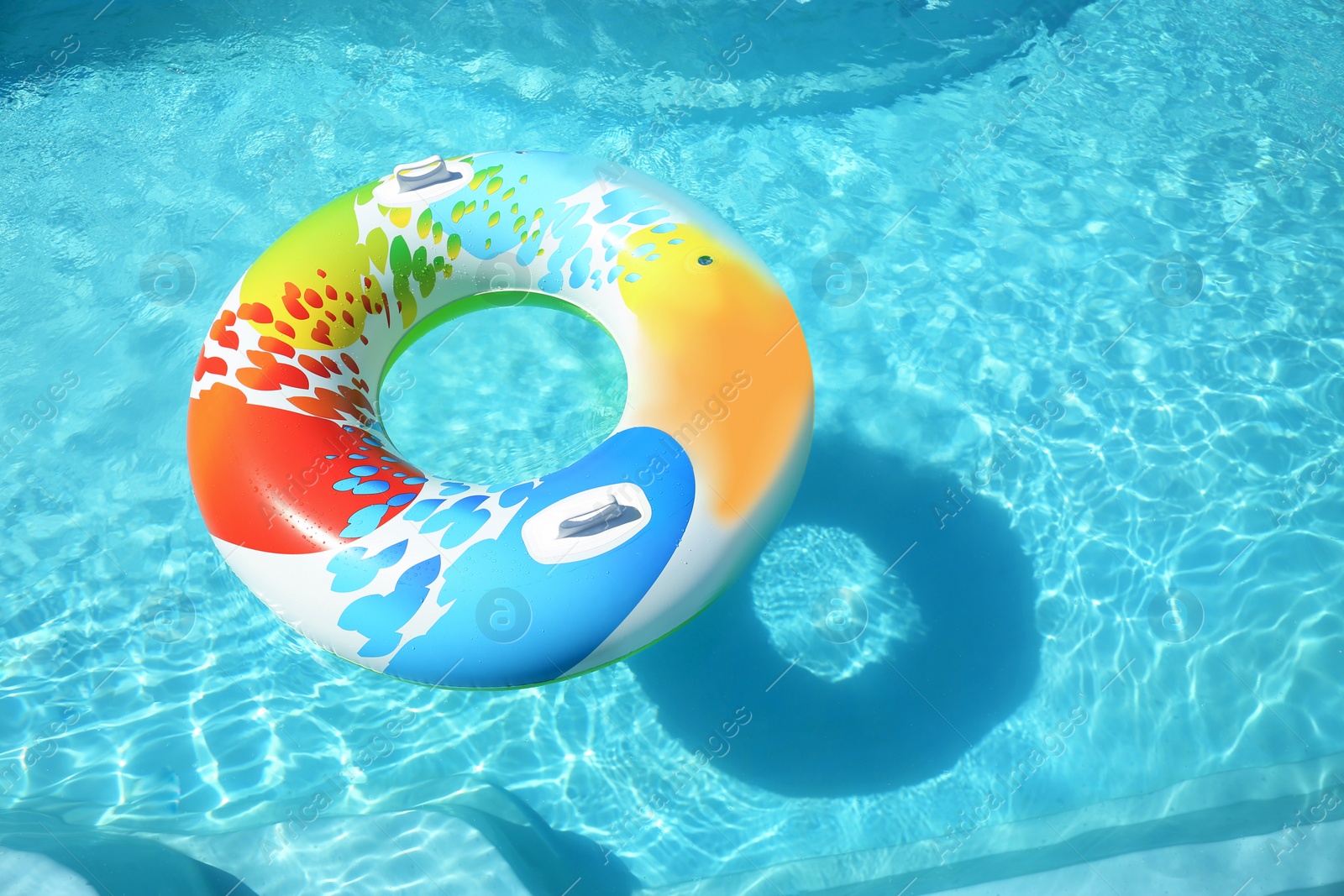 Photo of Colorful inflatable ring floating in swimming pool on sunny day. Space for text