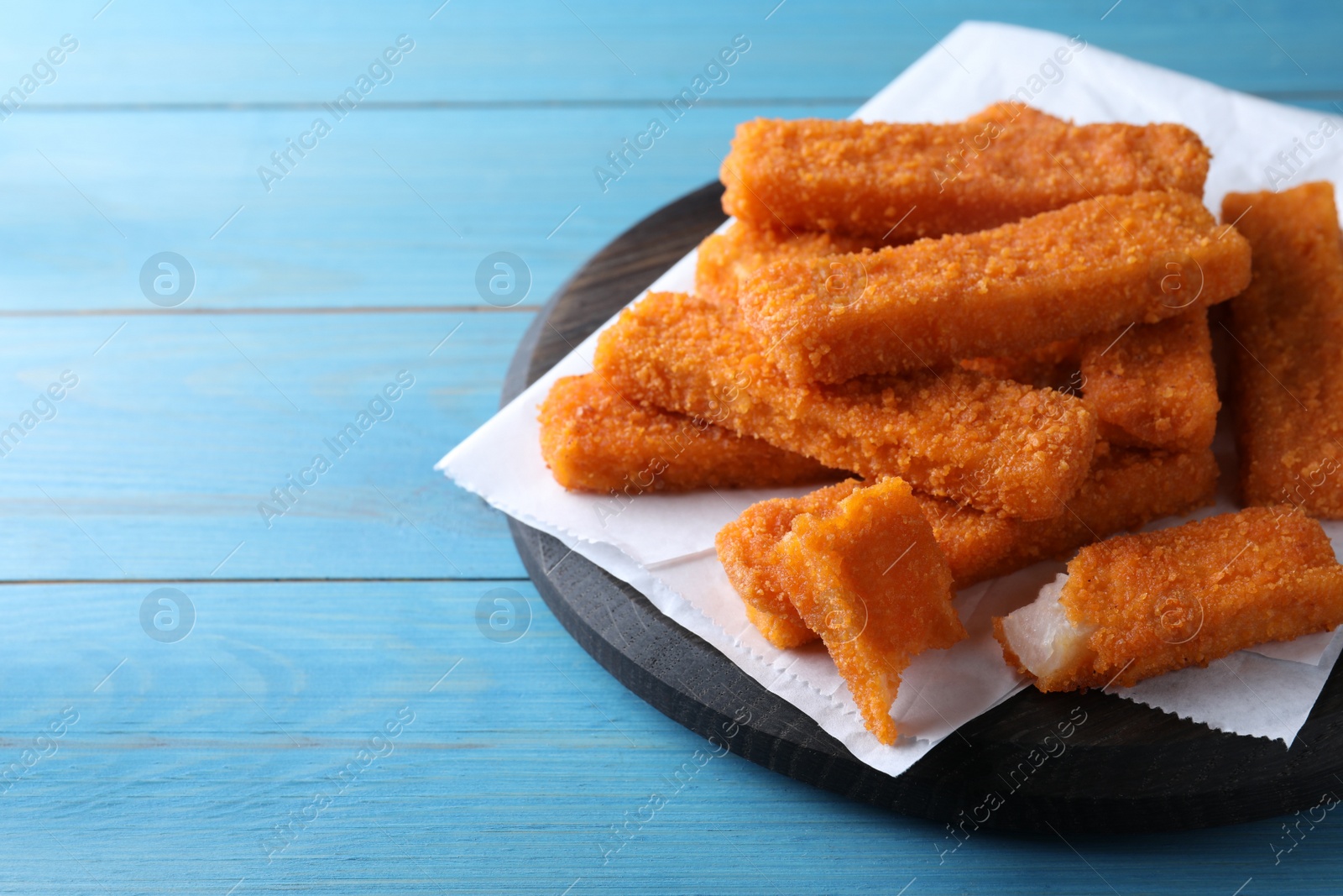 Photo of Fresh breaded fish fingers served on light blue wooden table, space for text