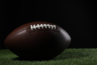 Photo of Leather American football ball on green grass against black background