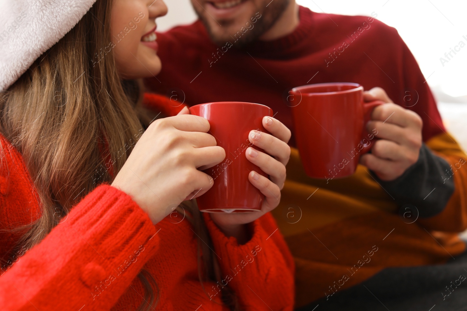 Photo of Happy young couple with cups of hot drink celebrating Christmas at home