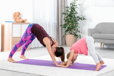 Sportive woman doing fitness exercises with daughter at home