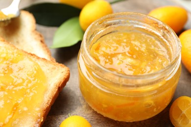 Photo of Delicious kumquat jam in jar, tasty toast and fresh fruits on wooden board, closeup