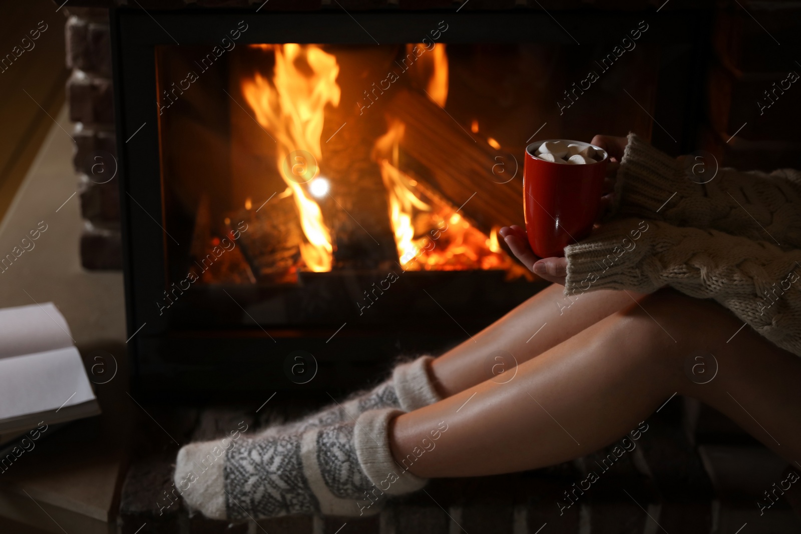 Photo of Woman with cup of delicious cocoa resting near fireplace at home, closeup. Winter vacation