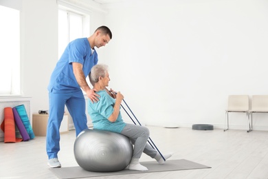 Professional physiotherapist working with elderly patient in rehabilitation center. Space for text