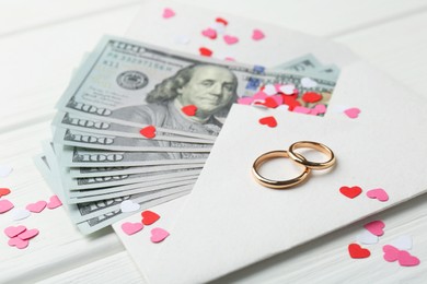 Photo of Honeymoon concept. Two golden rings, money and cutout hearts on white wooden table, closeup