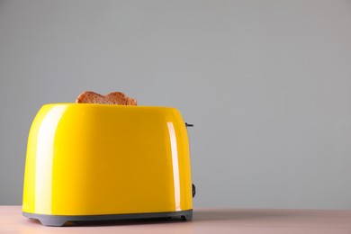 Modern toaster with slices of roasted bread on wooden table. Space for text