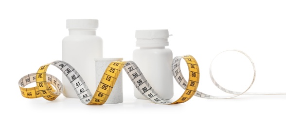 Photo of Bottles of weight loss pills and measuring tape isolated on white