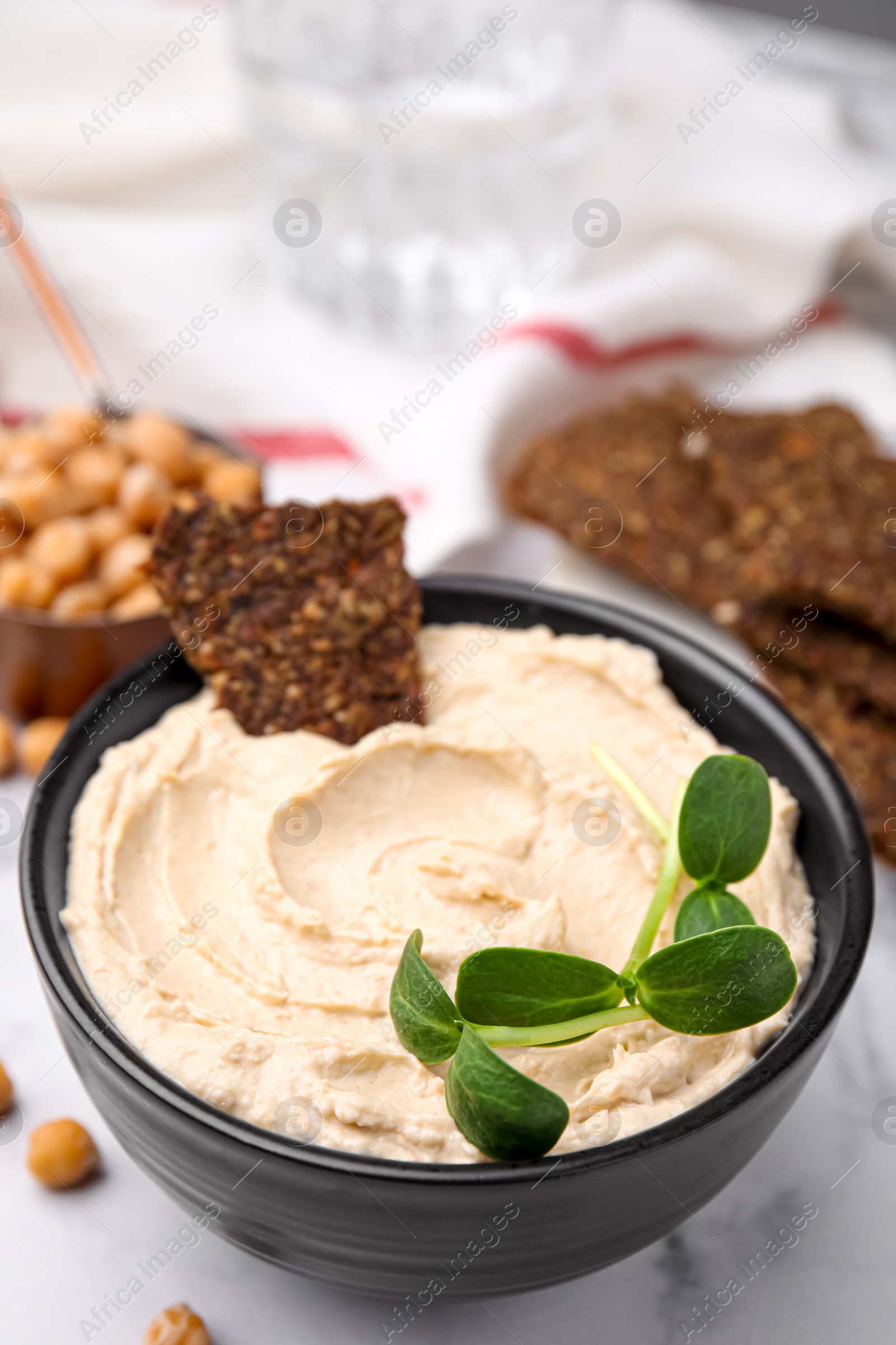 Photo of Delicious hummus with crispbread served on white marble table, closeup