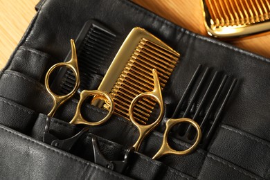 Photo of Hairdresser tools. Professional scissors and combs in leather organizer on wooden table, top view