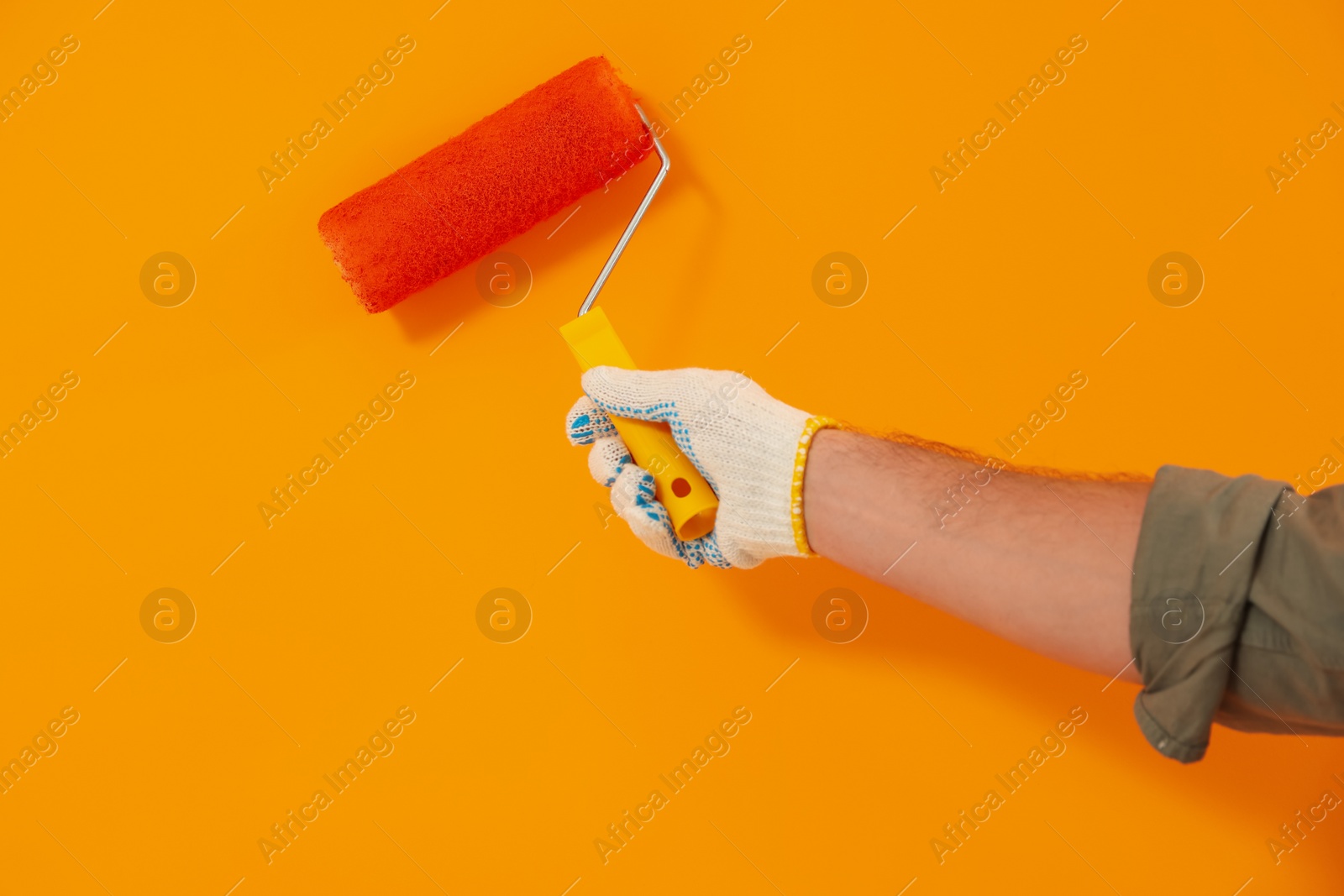 Photo of Designer painting orange wall with roller, closeup