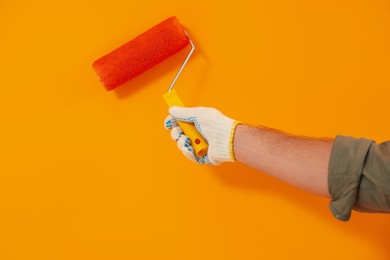 Photo of Designer painting orange wall with roller, closeup