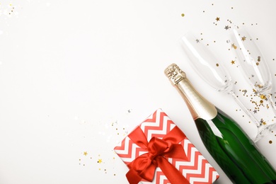 Photo of Creative flat lay composition with bottle of champagne, glasses and gift box on white background. Space for text