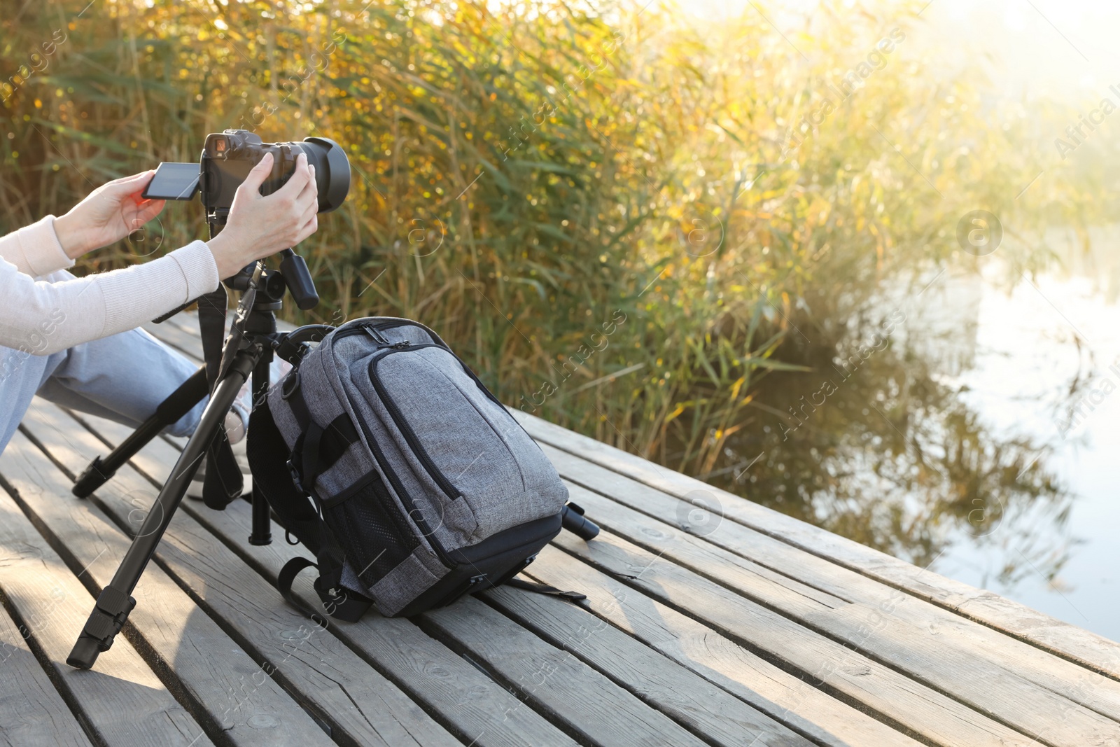 Photo of Photographer with tripod, modern camera and backpack on wooden pier