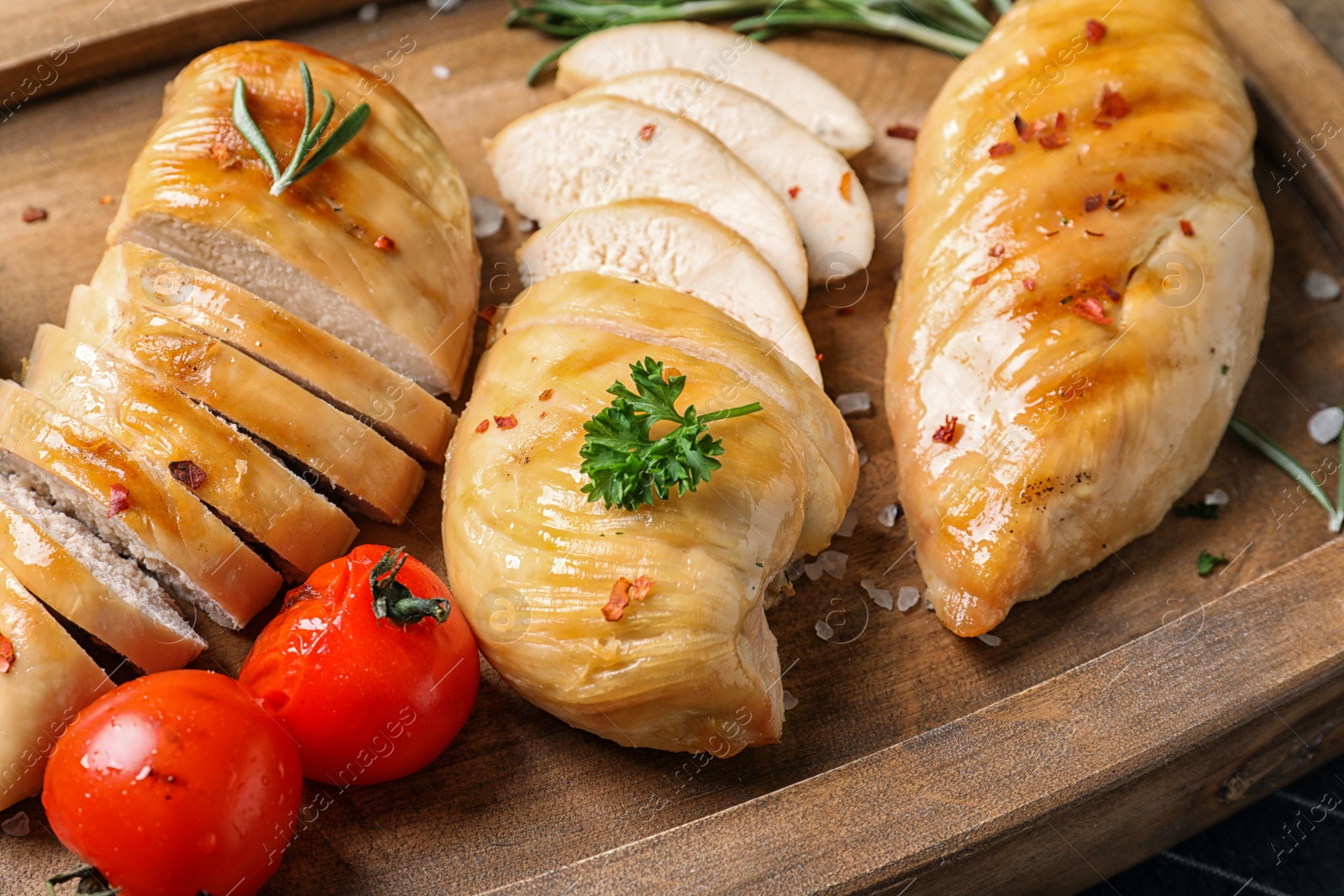 Photo of Fried chicken breasts and tomatoes served on wooden board, closeup