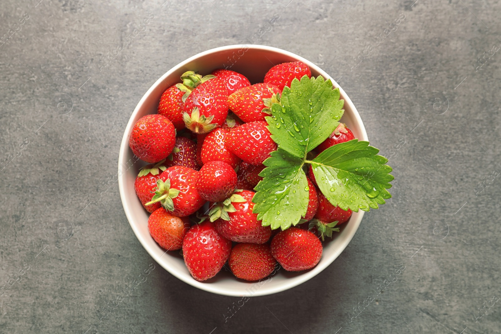 Photo of Bowl with ripe strawberries on grey background, top view