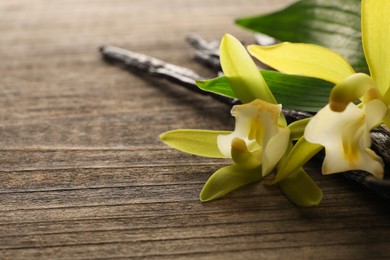 Vanilla pods, beautiful flowers and green leaves on wooden table, closeup. Space for text