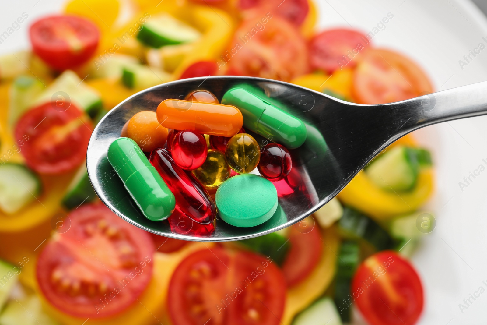 Photo of Spoon with weight loss pills over plate with vegetable salad, closeup