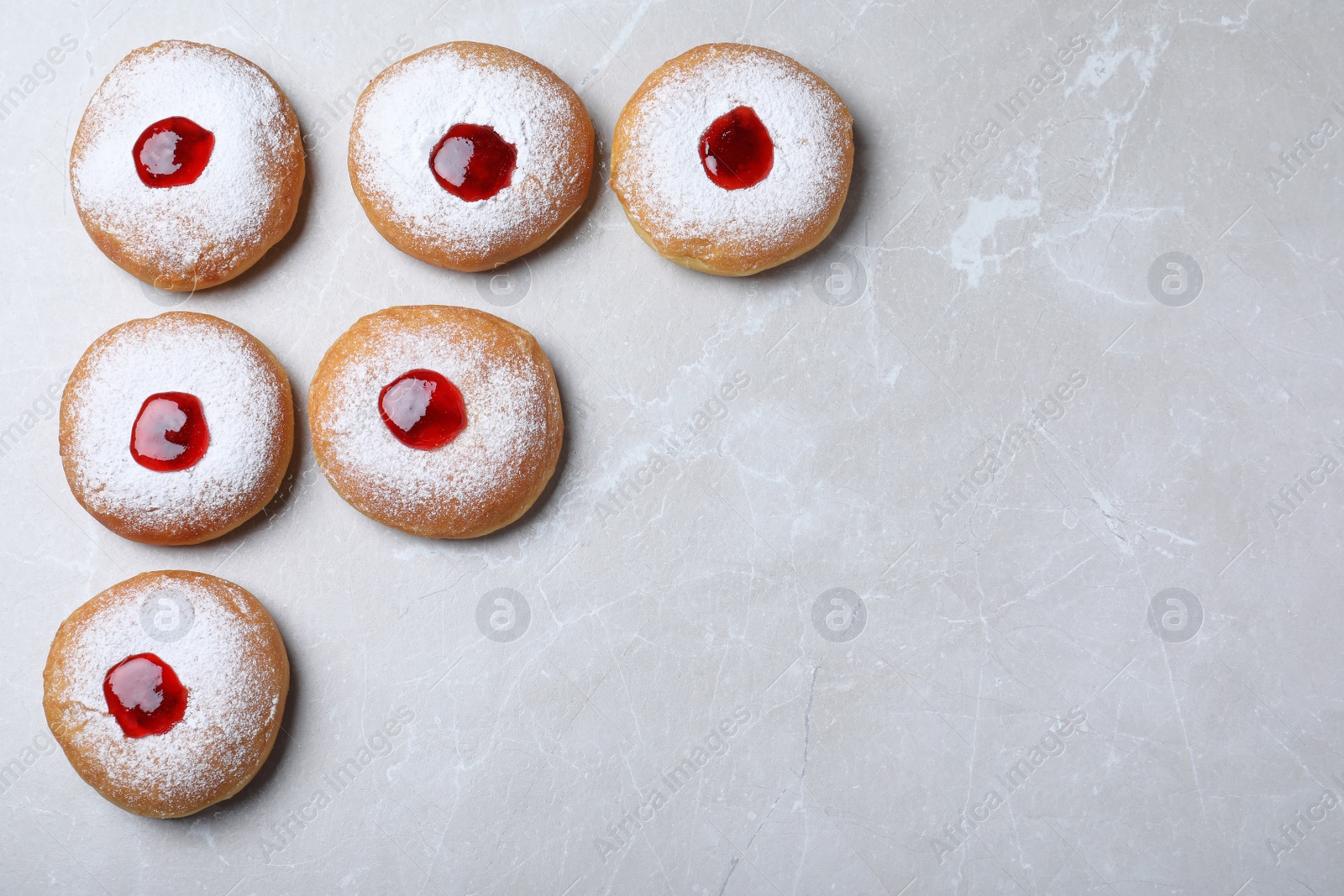 Photo of Hanukkah doughnuts with jelly and sugar powder on grey table, flat lay. Space for text