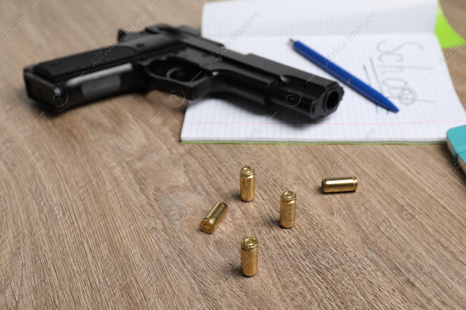 Photo of Gun, bullets and school stationery on wooden table, closeup