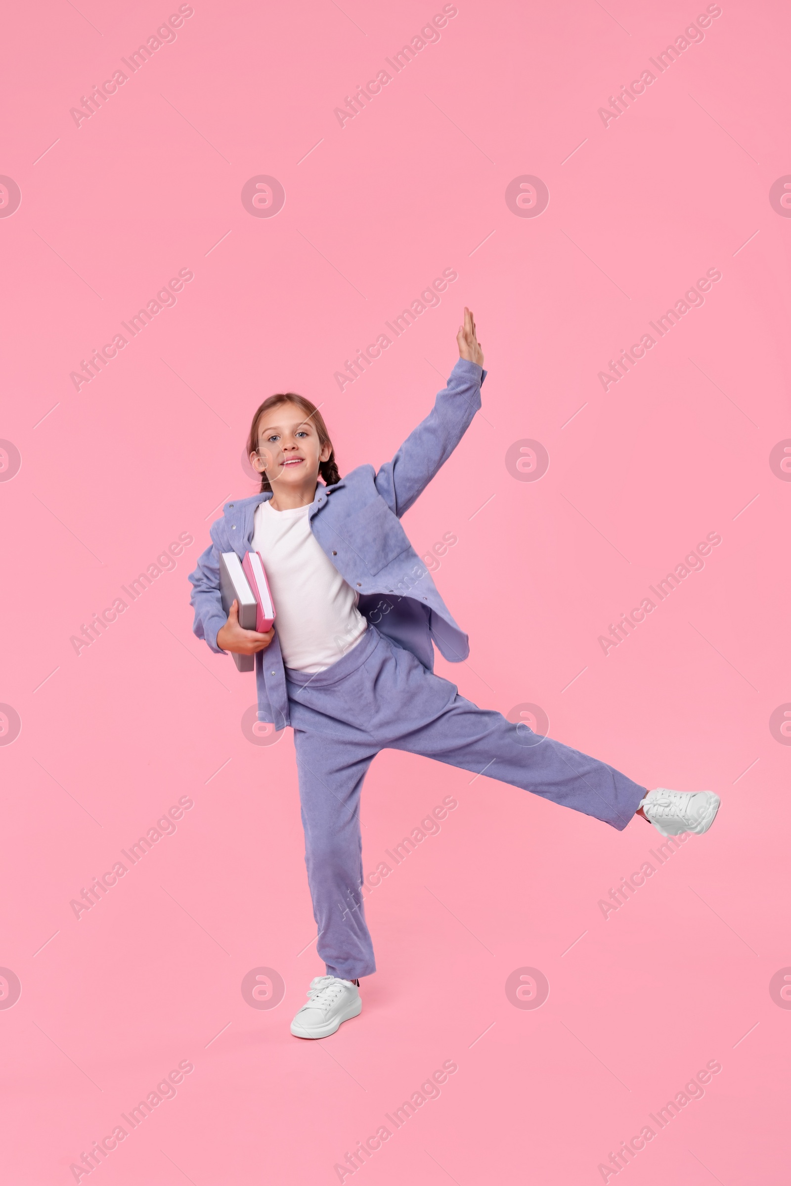 Photo of Smiling schoolgirl with books on pink background