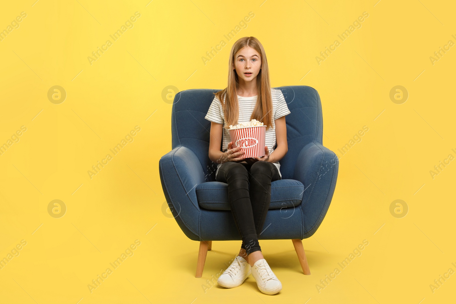 Photo of Emotional teenage girl with popcorn sitting in armchair during cinema show on color background