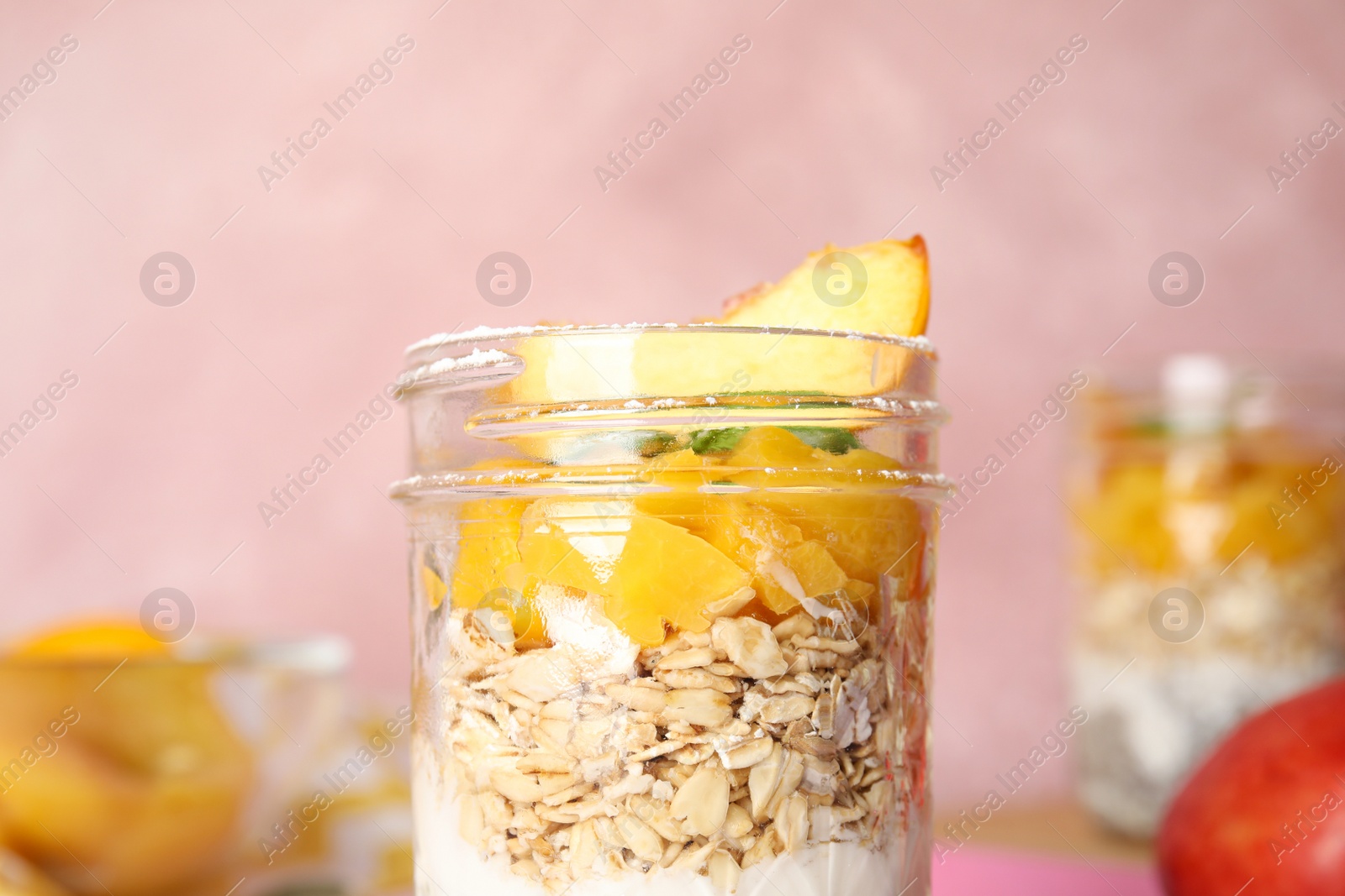 Photo of Tasty peach dessert with yogurt and granola on pink background, closeup