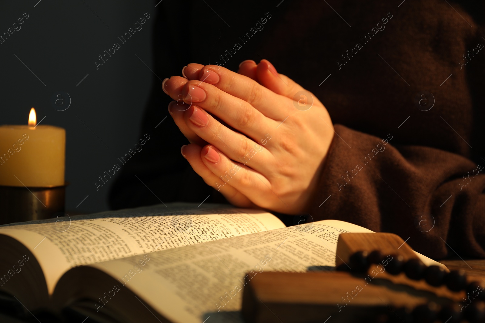 Photo of Woman praying at table with burning candle and Bible, closeup