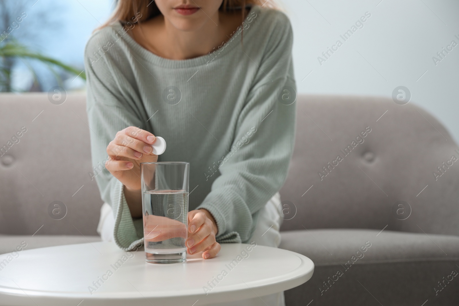 Photo of Woman putting medicine for hangover into glass of water at home, closeup