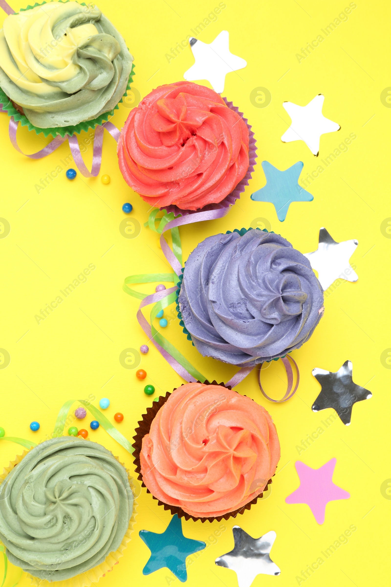 Photo of Delicious cupcakes with bright cream and party decor on yellow background, flat lay