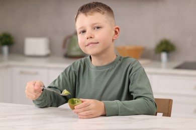 Boy with tasty fresh kiwi at white marble table in kitchen