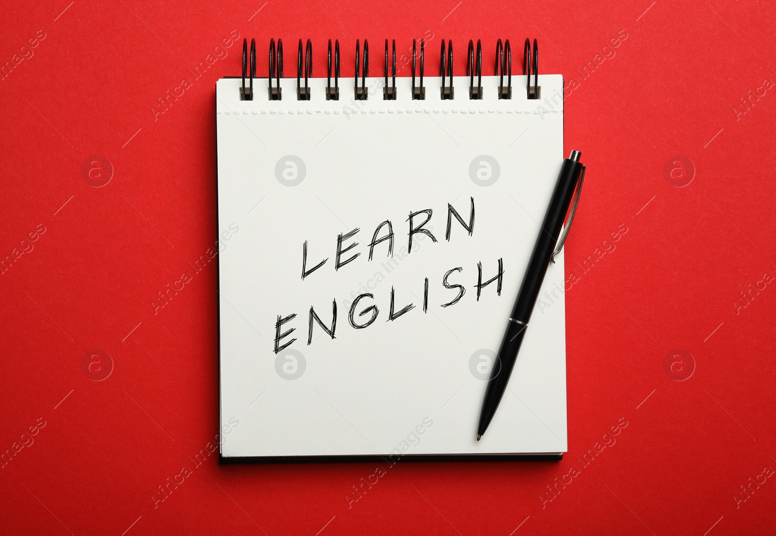 Image of Open notebook with text Learn English and pen on red background, top view