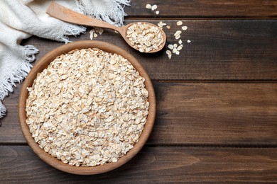 Photo of Bowl and spoon with oatmeal on wooden table, flat lay. Space for text